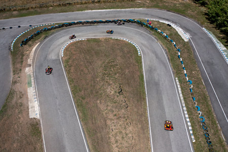Drone capturing go-karts moving on winding racetracks from top aerial perspective. Distant view of racing competition on road at countryside during daytimeの写真素材
