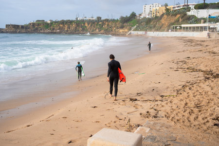 Anonymous surfers carrying surfboards as the walk along sandy seashore on beach, creating relaxed and vibrant coastal atmosphereの写真素材