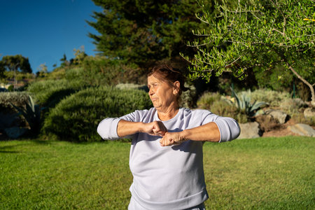 Elderly woman in sportswear exercising in park on a sunny day. Fit retired lady looking away, embracing an active and healthy lifestyle outdoorsの写真素材