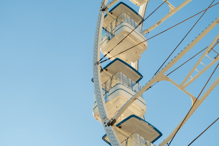 Ferris wheel with spacious white gondolas offering stunning views of the amusement park under sunny blue sky, captured from low angleの写真素材