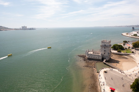 Aerial drone view of Belem Tower on Tagus River with boats creating wakes in the water, highlighting Lisbons scenic waterfront and historic architectureの写真素材