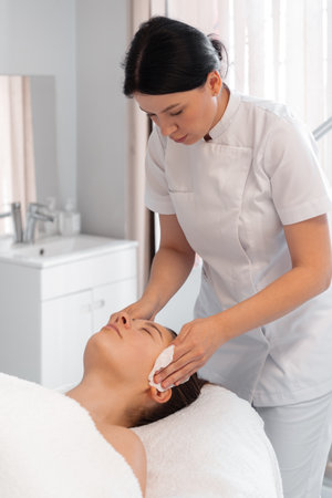 Cosmetologist wiping woman face with antibacterial napkins. Doctor performing beauty procedure in cosmetology clinic, cleaning the patients face for treatmentの写真素材
