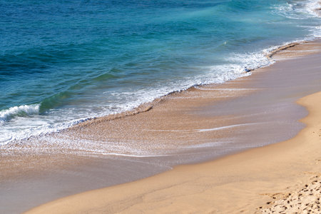 Soft beautiful ocean wave gently rolling onto sandy beach. Turquoise sea stretches out, creating a peaceful and serene coastal viewの写真素材