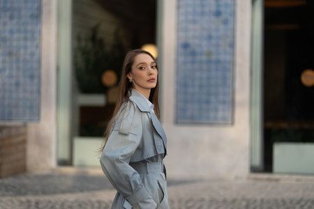 Side view of stylish young woman in blue outfit looking at camera. Beautiful lady with long hair...