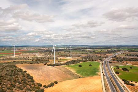 Drone shot of wind turbines spread across farmland with intersecting highways, under bright cloudy sky, showcasing sustainable energy in wide rural landscapeの写真素材