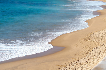 Soft beautiful ocean wave gently rolling onto sandy beach. Turquoise sea stretches out, creating a...