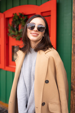 People, season and Christmas concept portrait of happy smiling middle age woman outdoors dressed stylish cream trench coat with Christmas festive decoration on background. Vertical photoの写真素材