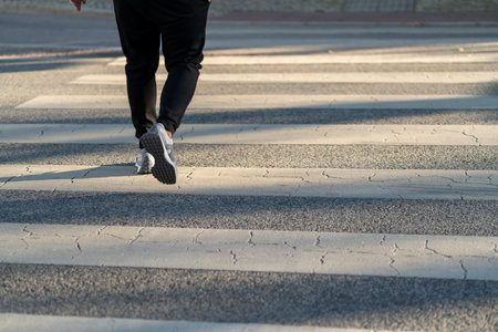Person is walking on a crosswalk in bright daylight. The pavement displays distinct shadow patterns...
