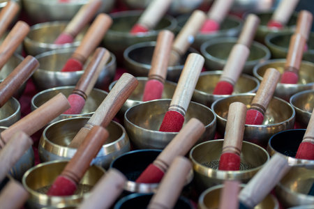 A bell vendor presents an array of handcrafted singing bowls in a vibrant market. Each bowl is...