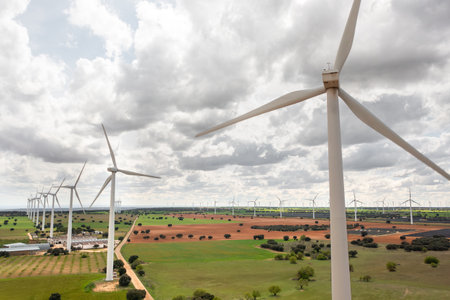 Wide view of large wind farm with turbines installed on green and brown farmlands under dramatic...