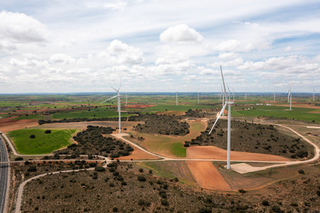Drone shot of wind turbines scattered across fields with winding dirt roads. Renewable energy...