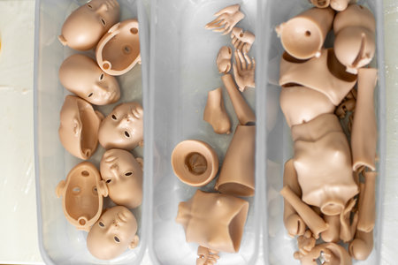 Closeup of silicone doll parts in containers, including faces, hands and body parts. Pieces are...