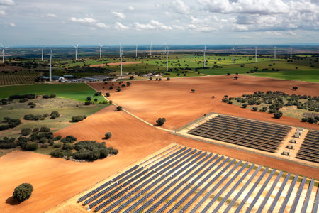 Aerial drone shot reveals solar panel farm in foreground and wind turbines in background,...