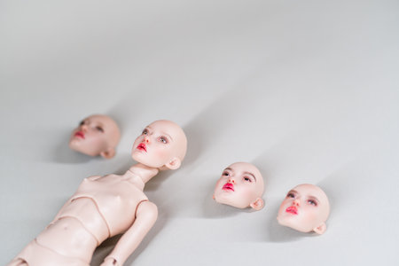 Doll body with multiple detachable heads on white background. Heads feature different facial...