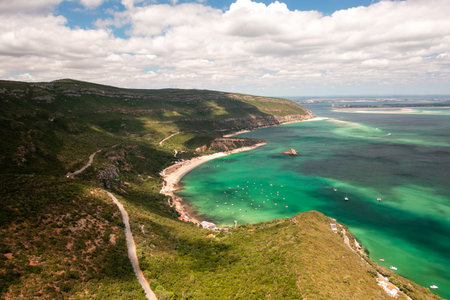 Drone footage showing Praia do Portinho da Arrabida with its turquoise waters and Convento de Nossa Senhora da Arrabida nestled in green mountains in Arrabida Natural Park, Portugalの写真素材