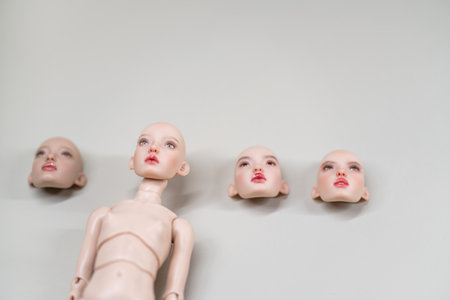 Ball jointed doll figure lying beside separate interchangeable heads on plain background, representing concept of customization and collectable doll hobbyの写真素材