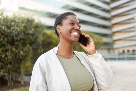 Smiling young businesswoman talking on smartphone near modern office building. Business, technology and people conceptの写真素材