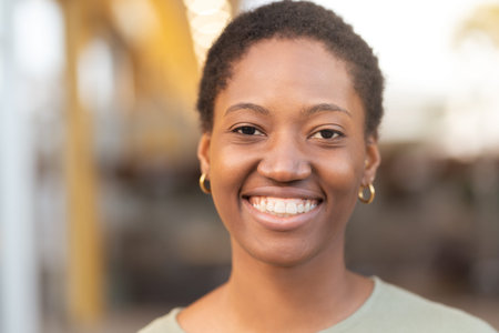 Smiling young Black woman with short hair. Closeup shot of female positive emotion looking at camera against blurred backgroundの写真素材