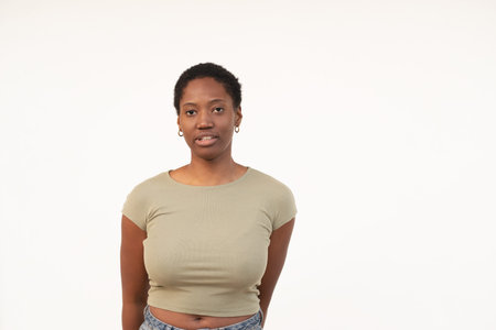 Portrait of young woman with short Afro hair standing against white background. Lady in casual clothes showing blank expression in white studioの写真素材