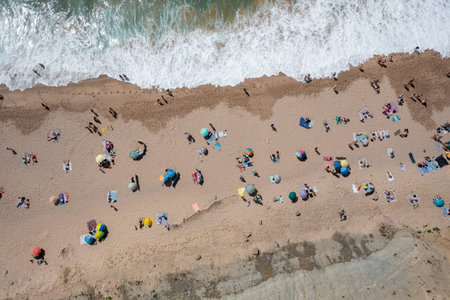 Overhead drone shot of tourists and colorful parasols on sandy seashore, showing people enjoying summer vacations at beach during sunny dayの写真素材
