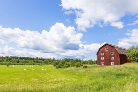 Scenic View of an Old Barn with White Silage Balls with a Blue Sky