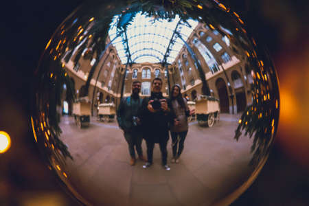 Silhouette of three friends enjoying time together while taking selfie of them reflected in a christmas silver ballの写真素材