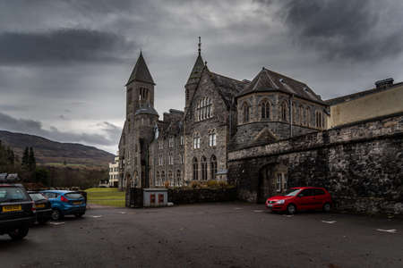 FORT AUGUSTUS, SCOTLAND, DECEMBER 17, 2018: The Abbey Highland Club, full of mold and lichen in its stone walls, under heavy cloudscape with mountains in the background, aside Loch Nessのeditorial素材
