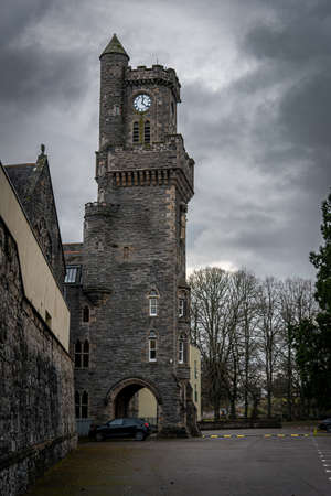 FORT AUGUSTUS, SCOTLAND, DECEMBER 17, 2018: The Abbey Highland Club clock tower, full of mold and lichen in its stone walls, under heavy cloudscape with mountains in the background, aside Loch Nessのeditorial素材