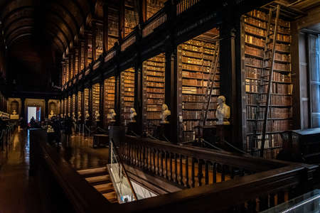 DUBLIN, IRELAND, DECEMBER 21, 2018: The Long Room in the Trinity College Library, home to The Book of Kells. Perspective view of the place, with large quantity of books and chest statuesのeditorial素材