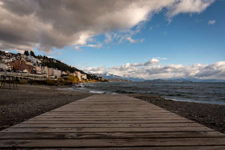 BARILOCHE, ARGENTINA, JUNE 18, 2019: Perspective view of the lake Nahuel Huapi and the cityscape, with snowed mountains in the background, seen from wooden deck of stony coastのeditorial素材