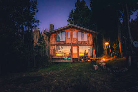BARILOCHE, ARGENTINA, JUNE 19, 2019: Exterior of a wooden cozy and relaxing cabin in the forest during the last moments of light with sunset reflecting on its windowsのeditorial素材