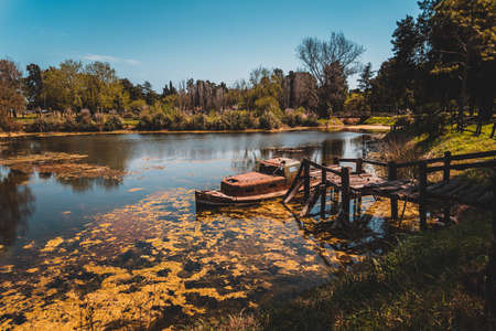 Old rusty abandoned wrecked ship tied up to a broken wooden dock in a small lake.の写真素材
