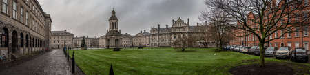 DUBLIN, IRELAND, DECEMBER 21, 2018: Panoramic view of Trinity College and its interior park, full of green grass surrounded by cobbled stone streets being separated by a long chain during a rainy dayのeditorial素材