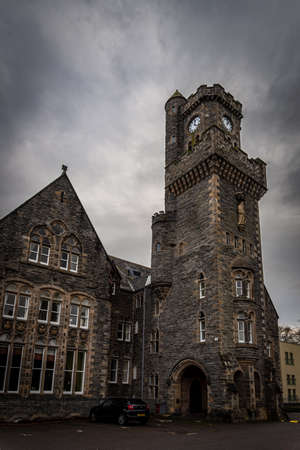 FORT AUGUSTUS, SCOTLAND, DECEMBER 17, 2018: The Abbey Highland Club clock tower, full of mold and lichen in its stone walls, under heavy cloudscape with mountains in the background, aside Loch Nessのeditorial素材