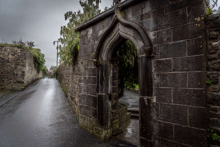 KILKENNY, IRELAND, DECEMBER 23, 2018: Spooky old stone and very wet entrance gate of a graveyard with mold and lichen growing. Concept of desolation and damageのeditorial素材