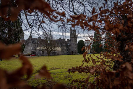 FORT AUGUSTUS, SCOTLAND, DECEMBER 17, 2018: The Abbey Highland Club clock tower and its garden, across leaves of trees, under heavy cloudscape with mountains in the background, aside Loch Nessのeditorial素材