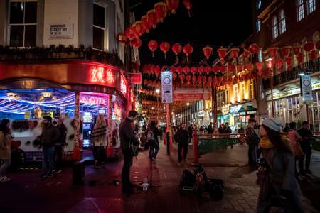 LONDON,ENGLAND,DECEMBER 10th, 2018: street musician playing the guitar under neon lights in Chinatown, decorated by Chinese lanterns during christmas and new year while people is passing by Wardour Stのeditorial素材