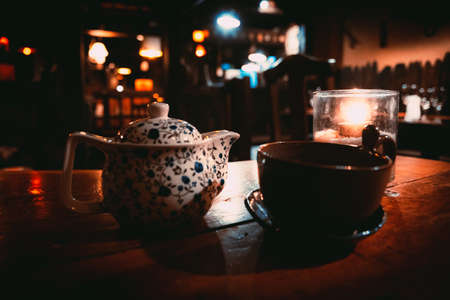 A teapot, a cup and a tealight inside a glass over a wooden table of a cozy Irish pub.の写真素材
