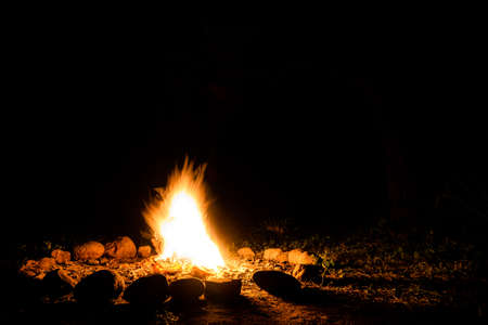 Flames of a campfire in deep darkness surrounded by stones shaping strong shadows. Space for inserting textの写真素材