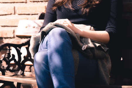Close up of womans hands resting over her crossed legs while being sit on a bench in a sunny dayの写真素材