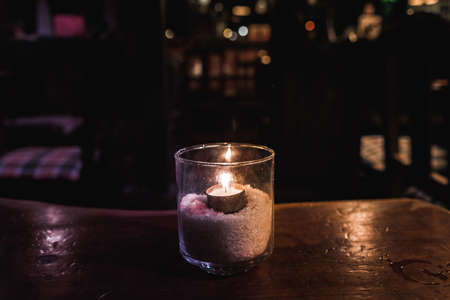 Isolated tealight inside a glass illuminating a dark scene and reflections on a wooden table and a nice bokeh backgroundの写真素材
