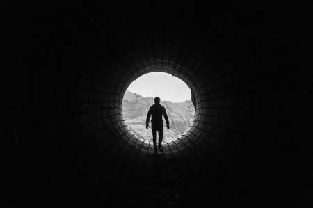 Silhouette of a man walking to the light at the end of a big tunnel. Concept of escape, exit, freedom, clinical deathの素材 [FY310158899182]