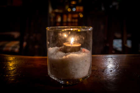 Isolated tealight inside a glass illuminating a dark scene and reflections on a wooden table and a nice bokeh backgroundの写真素材