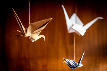 Deep bokeh of three origami swans hanging from the roof with a wooden backgroundの写真素材