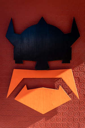 Minimalist Viking head carved in wood, with black helmet and orange beard, hung on red textured wallの写真素材