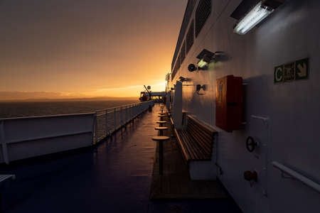 Deck of ferry sailing across the sea during last moments of a beautiful sunset with arriving land in the background. Concept of relaxation, adventure, freedom, luxury and leisure.の写真素材