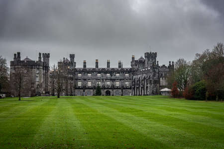 KILKENNY, IRELAND, DECEMBER 23, 2018: Kilkenny Castle seen from the huge garden on a dramatic cloudy day with dry leaves over the green grass.のeditorial素材