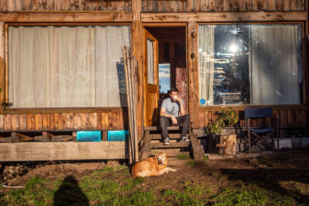 BARILOCHE, ARGENTINA, JUNE 19, 2019: Friendly dog waiting for its master outside the doorway of a cabin in the forest on a shiny bright sunny day while he drinks a cup of coffee.のeditorial素材