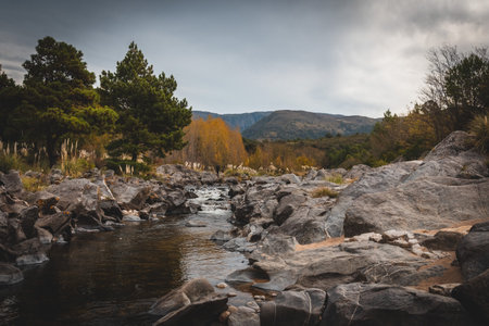 Mountain river view with trees surrounding the water while a man is fishing at San Clemente in Cordoba, Argentinaの写真素材