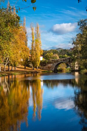Fall foliage and medieval Roman bridge reflected on the water in the Galician village of Allariz, Ourense.の写真素材